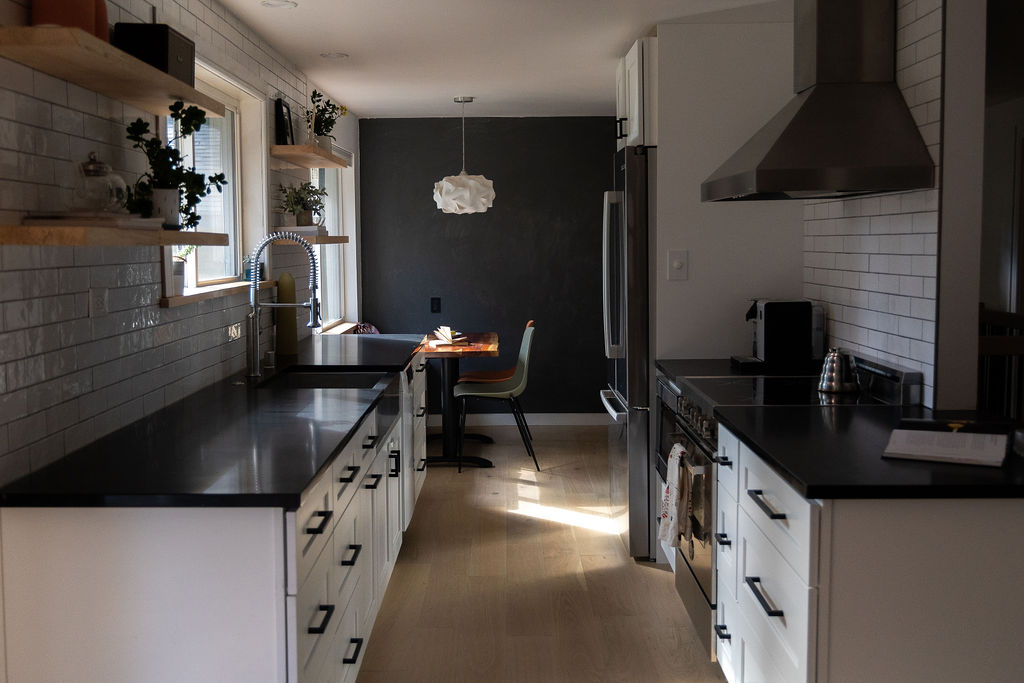A modern galley kitchen remodel ideas gallery featuring a long run of white cabinets, matte black countertops, a stainless steel apron-front sink, and warm wood floating shelves for a balanced, high-contrast look.