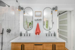 Luxury bathroom interior featuring dual oval mirrors, wood cabinetry, and a walk-in marble shower, illustrating high-end finishes for estimating bathroom remodel cost.