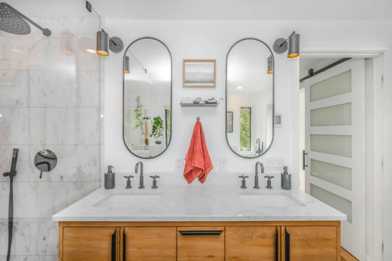 Luxury bathroom interior featuring dual oval mirrors, wood cabinetry, and a walk-in marble shower, illustrating high-end finishes for estimating bathroom remodel cost.