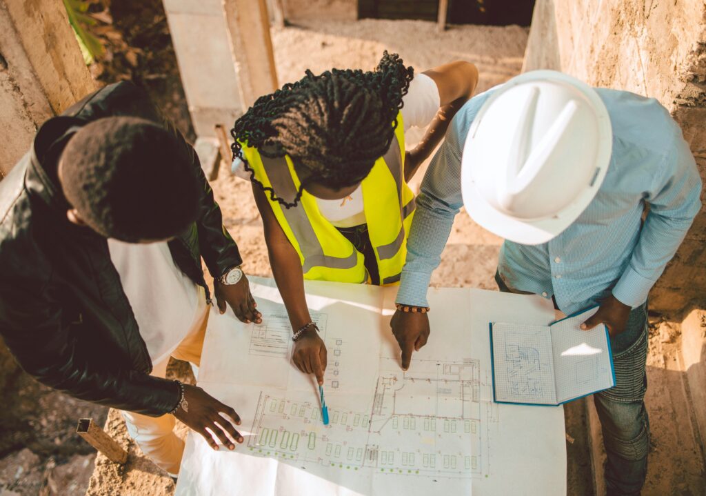 Three professionals reviewing architectural blueprints on a construction site, illustrating the collaborative roles of a contractor vs architect vs builder during a home renovation.