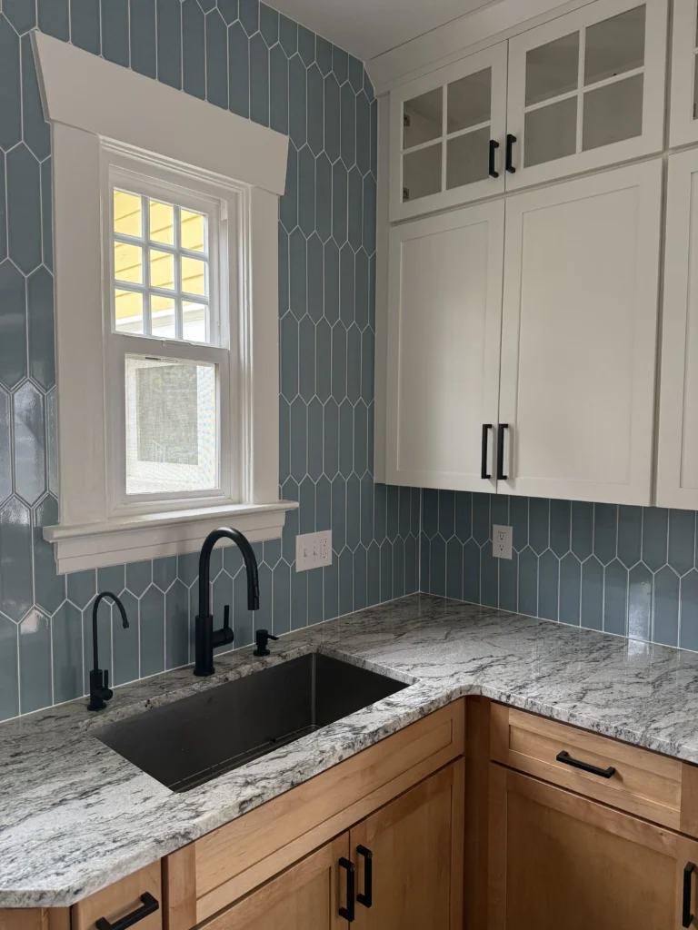 Modern open concept kitchen remodel showcasing a blue picket tile backsplash, granite countertops, and two-tone cabinetry with matte black fixtures.