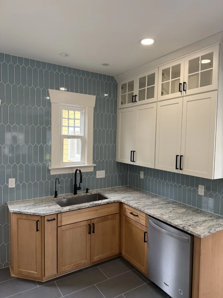 Modern open concept kitchen remodel featuring a blue picket tile backsplash, granite countertops, and two-tone cabinetry with a farmhouse-style sink.