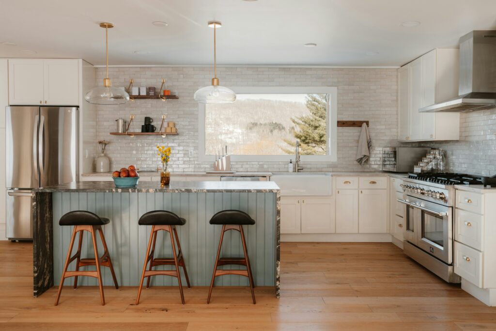 Modern kitchen with white cabinets, a light blue island, and a window view, showing high-quality design choices that avoid remodeling mistakes.