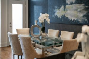 A modern dining room with a glass-top table, quilted chairs, and a decorative silver vase, showcasing the final results delivered by a professional home remodeling contractor.