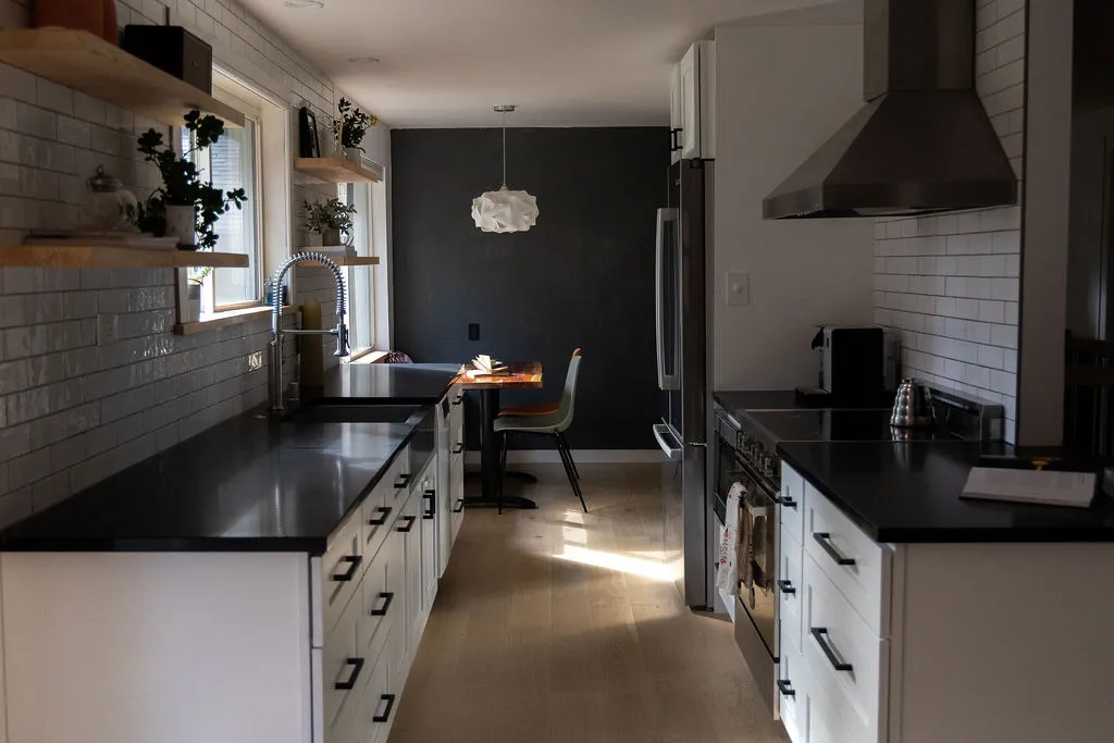Modern galley kitchen showcasing a high-end remodel with sleek black countertops, white shaker cabinets, subway tile backsplash, and stainless steel range hood.