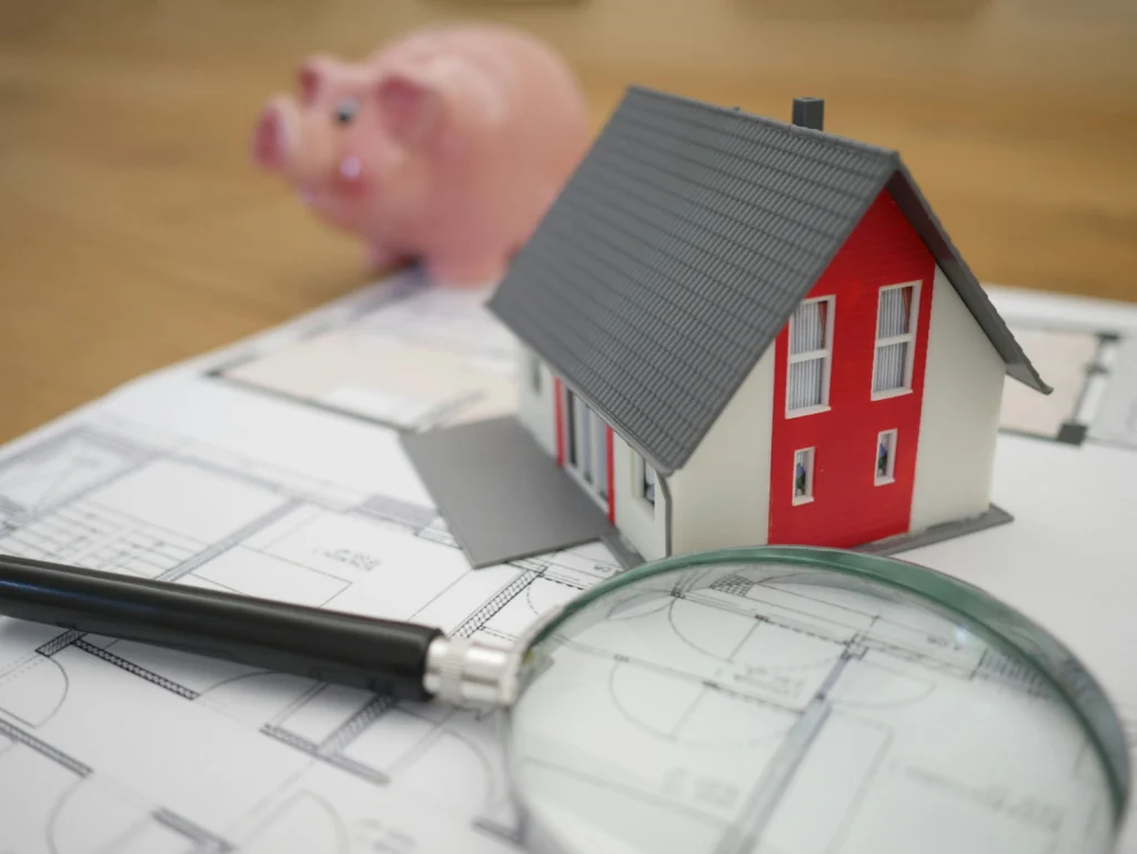 Architectural blueprints with a miniature house and magnifying glass used to calculate costs and set a realistic kitchen remodel budget.