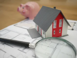 Architectural blueprints with a miniature house and magnifying glass used to calculate costs and set a realistic kitchen remodel budget.